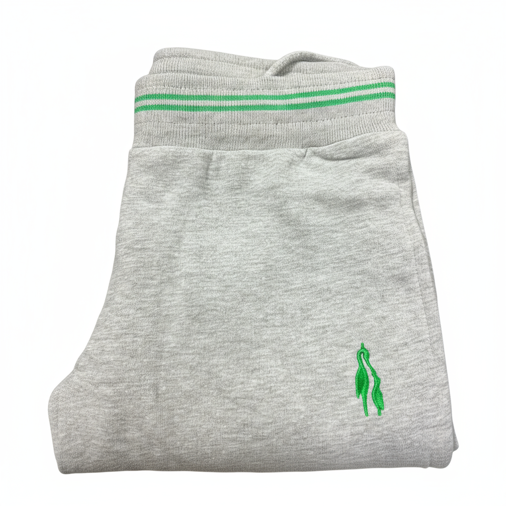 Grey sports trousers with green stripes and a logo on the left leg, displayed in a packed state with a visible green and white striped fabric on top.