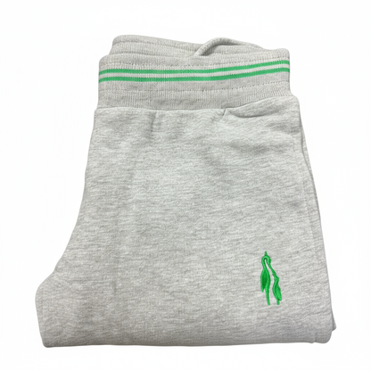 Grey sports trousers with green stripes and a logo on the left leg, displayed in a packed state with a visible green and white striped fabric on top.